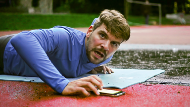 Ein Mann liegt auf einer Trainingsmatte und startet die Stoppuhr auf seinem Handy.