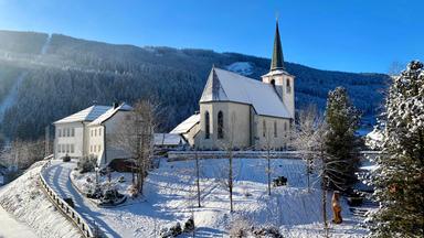 Eine Kirche und Häuser verschneit vor blauem Himmel