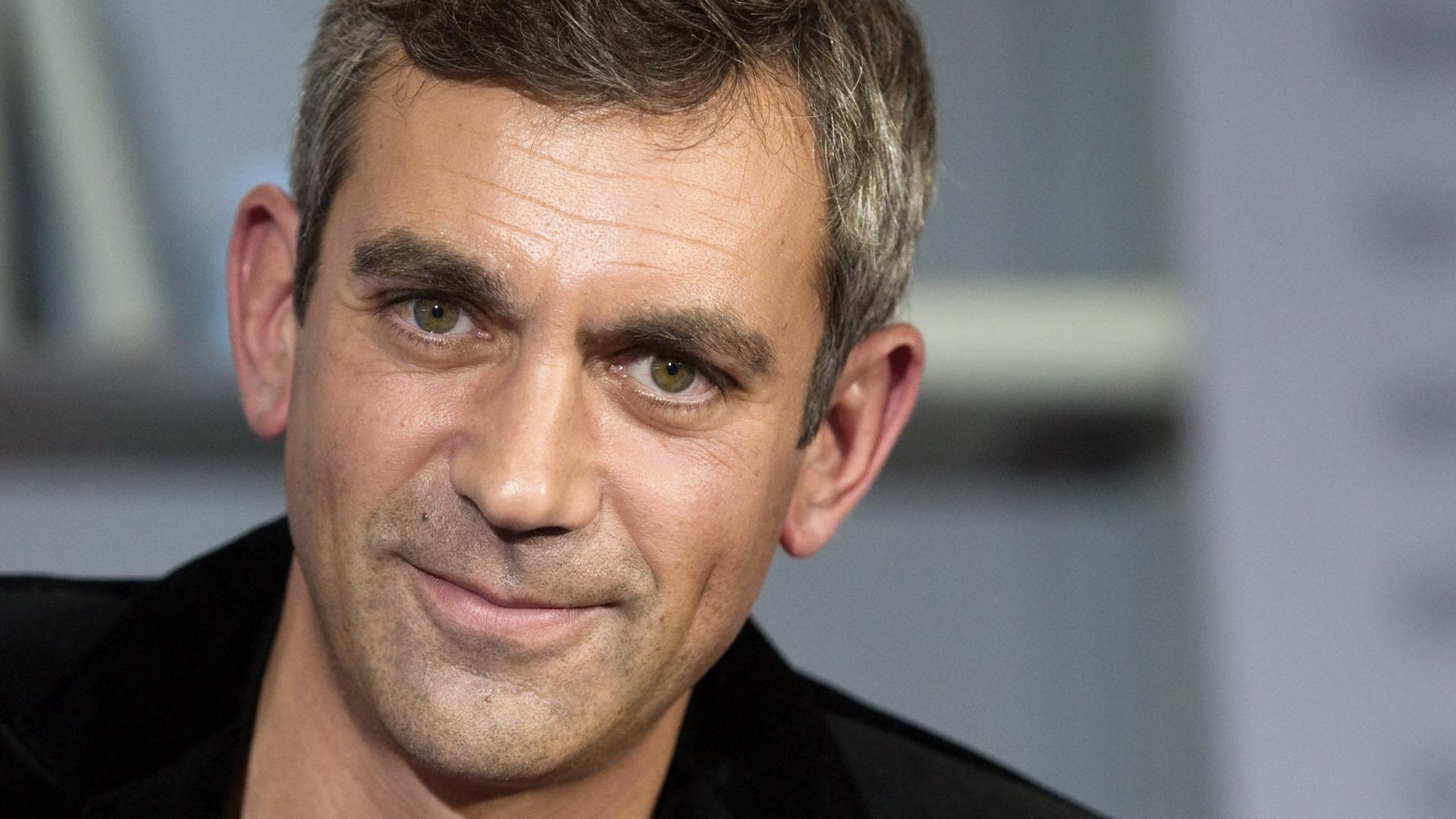 Ein Mann mit großen Augen lächelt mit geschlossenem Mund in die Kamera.