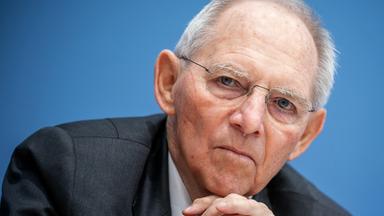 Ein Mann mit randloser Brille und kurzem grauen Haar stützt sein Kinn auf seinen Händen ab und blickt ernst in die Kamera.