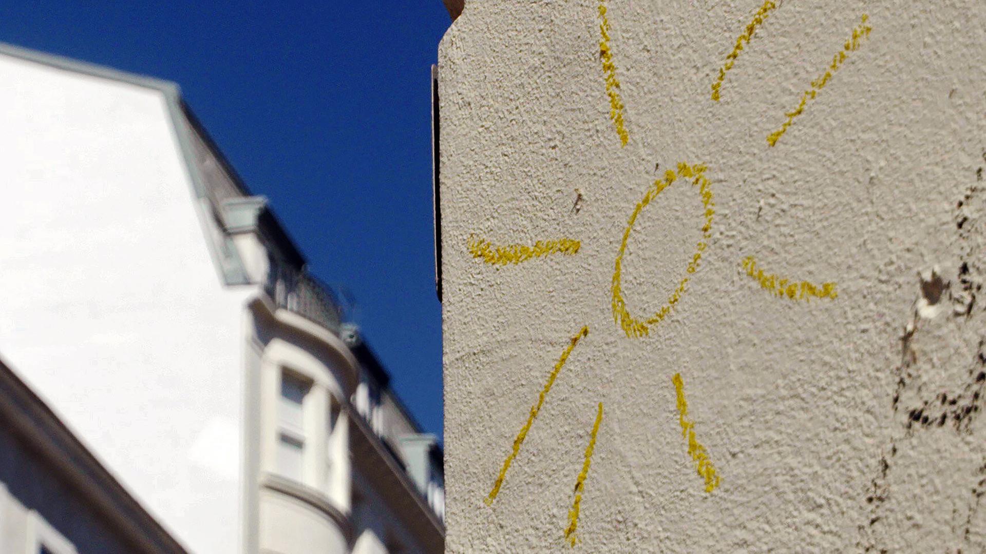 Eine gemalte gelbe Sonne auf einer hellen Hauswand.