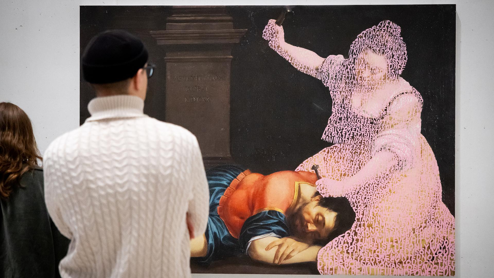 Ein Paar schaut sich ein großformatiges Bild an, auf dem ein Mann in historischer Kleidung schlafend auf dem Boden liegt, während eine Frau, die nur als verwitterter Umriss zu sehen ist, über ihm kniet und mit einer Hand ausholt.