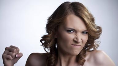 Eine junge Frau mit freiem Dekolleté ballt eine Faust und verzieht wütend das Gesicht.