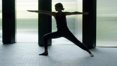 Eine Frau in Yoga-Position als Silhouette vor einem großen Fenster.