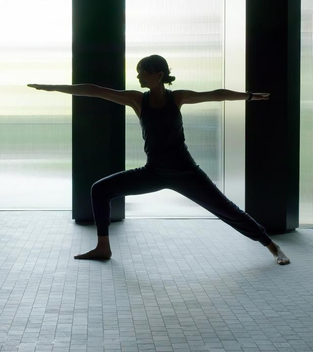 Eine Frau in Yoga-Position als Silhouette vor einem großen Fenster.