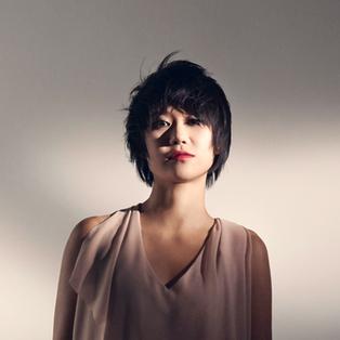 Eine Frau steht in einem hellen Kleid vor einer weißen Wand.