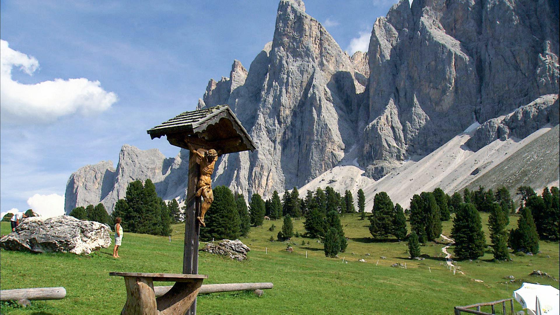 Wegkreuz mit Jesusfigur auf Wanderweg vor steil aufragenden Gipfeln