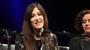 Eine Frau mit langen Haaren spricht in ein Mikrofon.