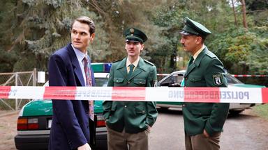 Drei Männer stehen hinter eine Absperrung, zwei davon tragen eine Polizeiuniform.