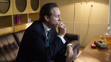 Ein Mann sitzt auf einer Couch. Er raucht eine Zigarette.