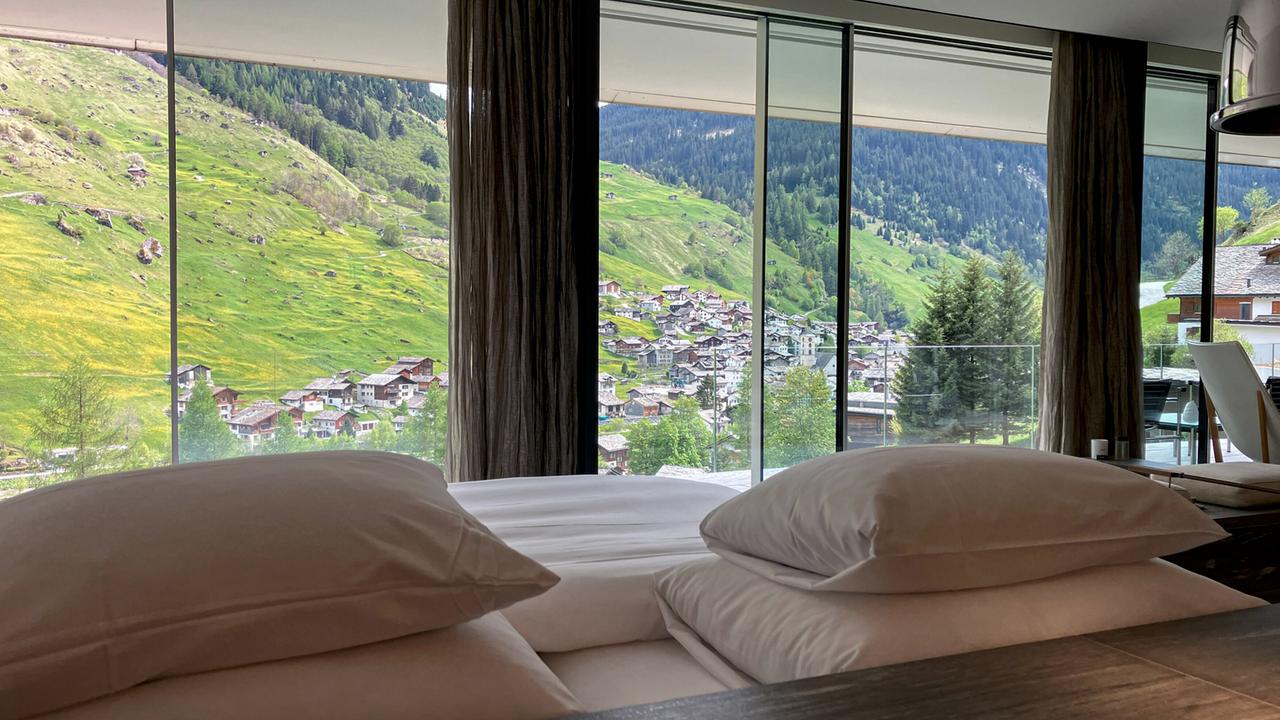 Blick aus einem Hotelzimmer mit frisch bezogenem Bett auf ein Ortspanorama