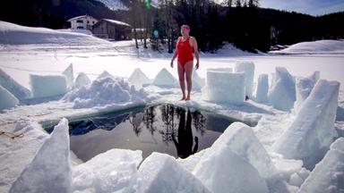 Eine Frau steht vor einem Loch in einem eingefrorenen See im Badeanzug.